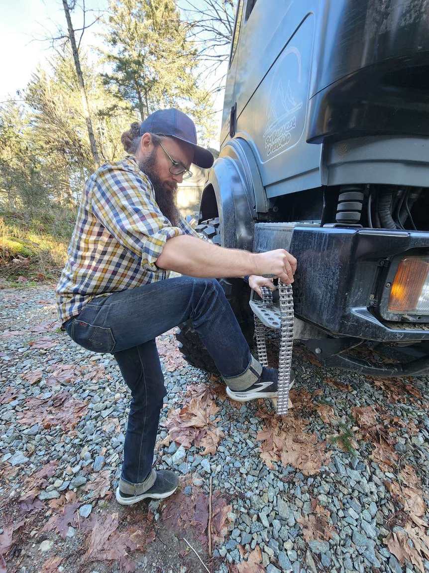 Guest fitting tire chains on an expedition truck on a gravel road