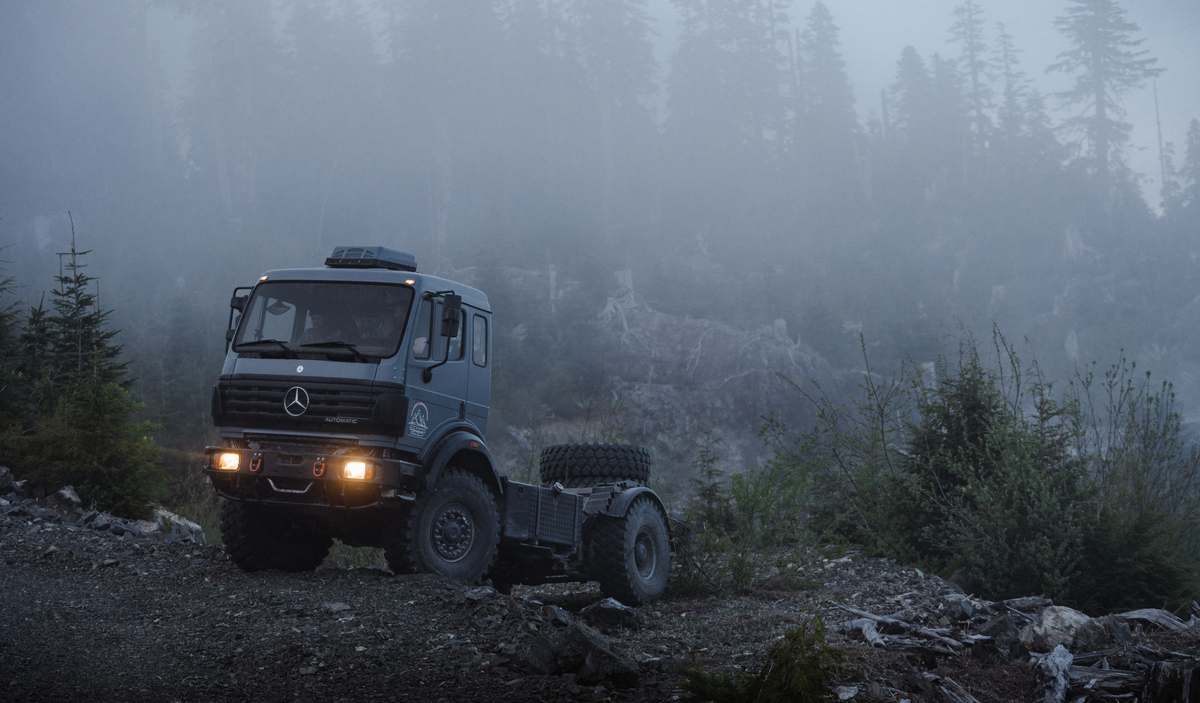 Mercedes-Benz expedition truck with headlights on in a misty mountain forest