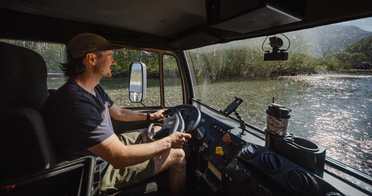 View from the driver seat of an expedition truck, forest road and lake through the windshield