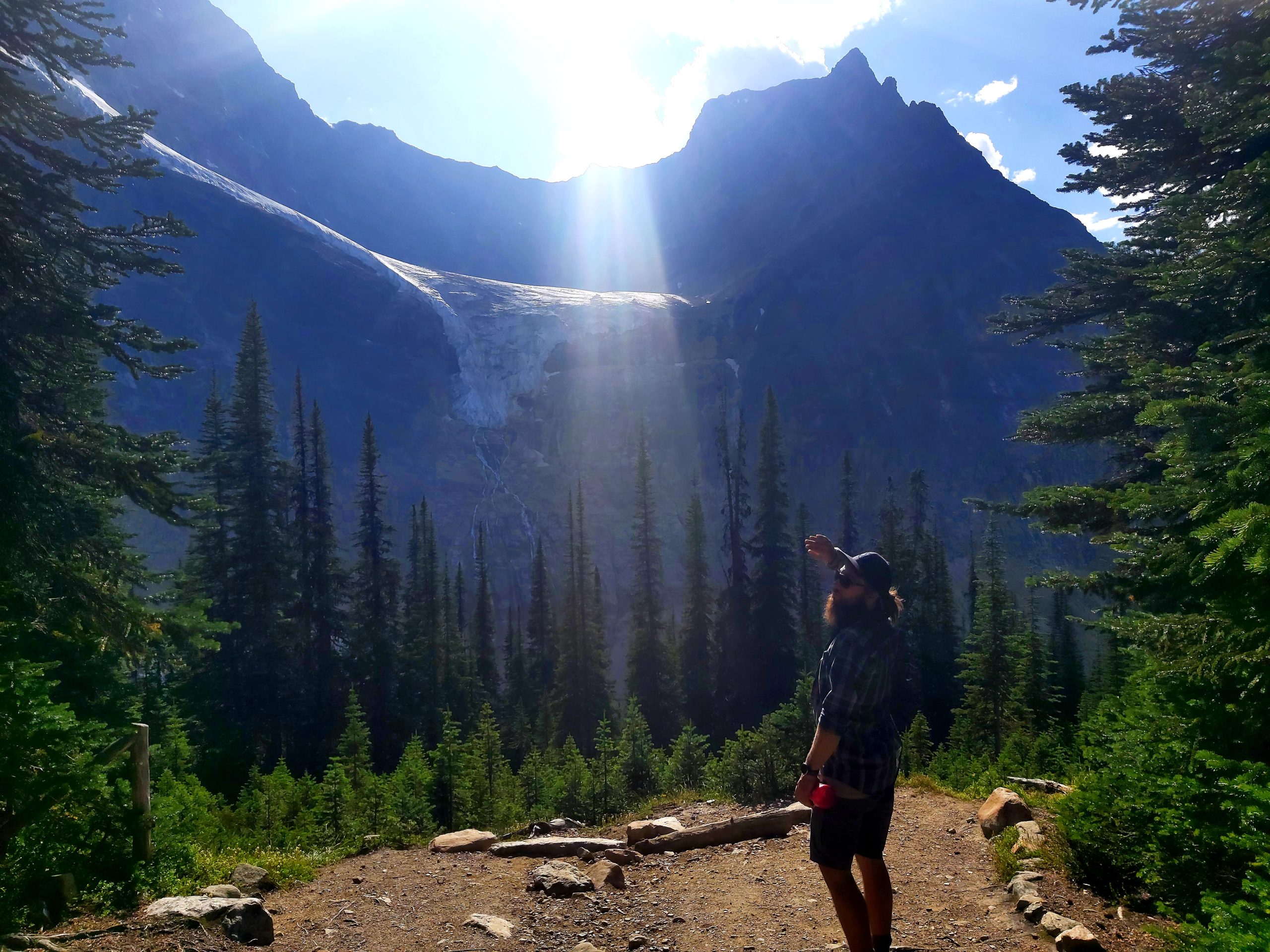Man points toward a glacier under sunbeams in the Canadian Rockies, symbolizing the spirit behind Canadian overland trucks